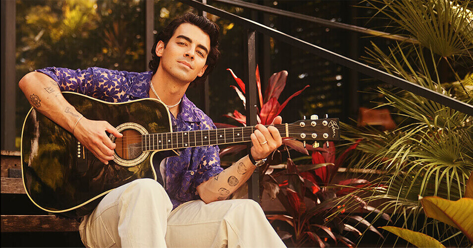 Joe jonas sitting on the stairs and playing guitar outside